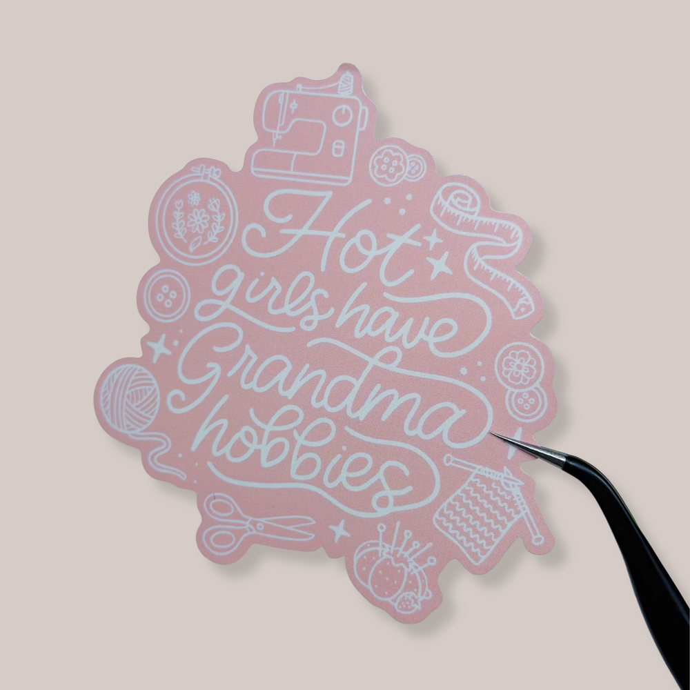 Pink decorative item with text and sewing-themed illustrations on a beige background