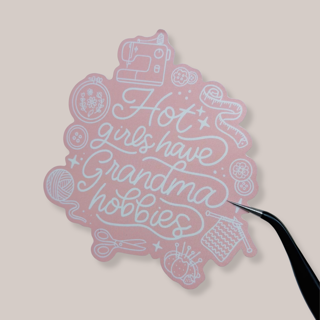 Pink decorative item with text and sewing-themed illustrations on a beige background