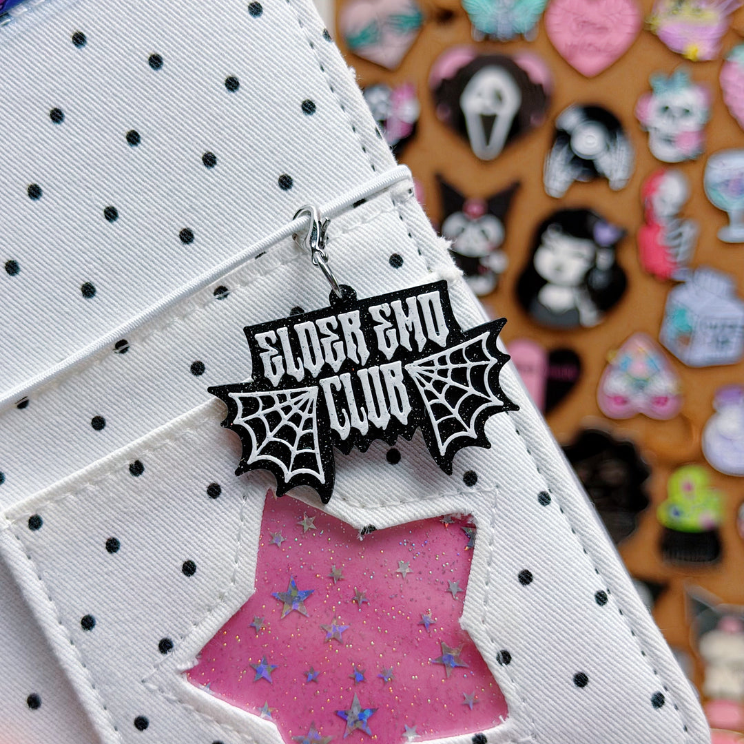 Black 'Elder Emo Club' spider web design on a polka dot background with other decorative items in the background.
