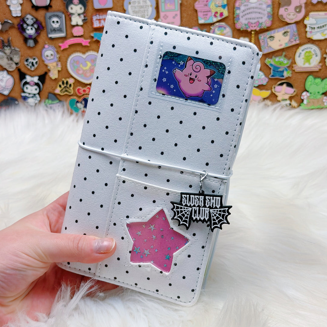 White polka dot wallet with decorative stickers held by a hand on a fluffy white surface.