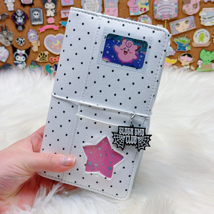 White polka dot wallet with decorative stickers held by a hand on a fluffy white surface.