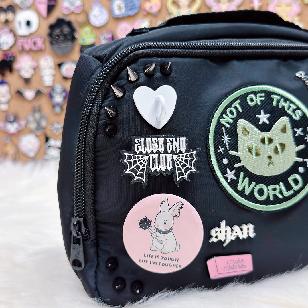 Black bag with various stickers and pins on a textured surface with a colorful background.