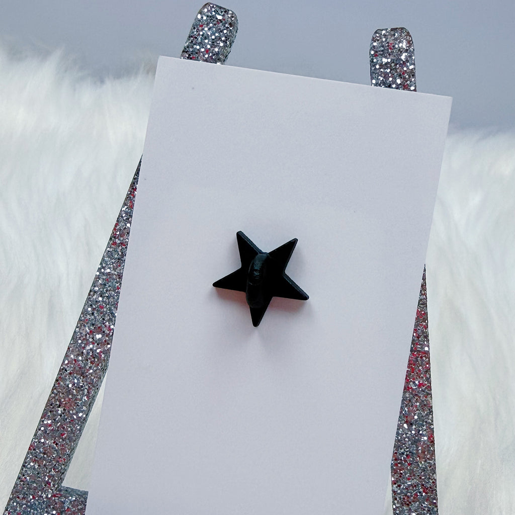 Black star-shaped earring on a white card with glittery silver stands against a light gray background.