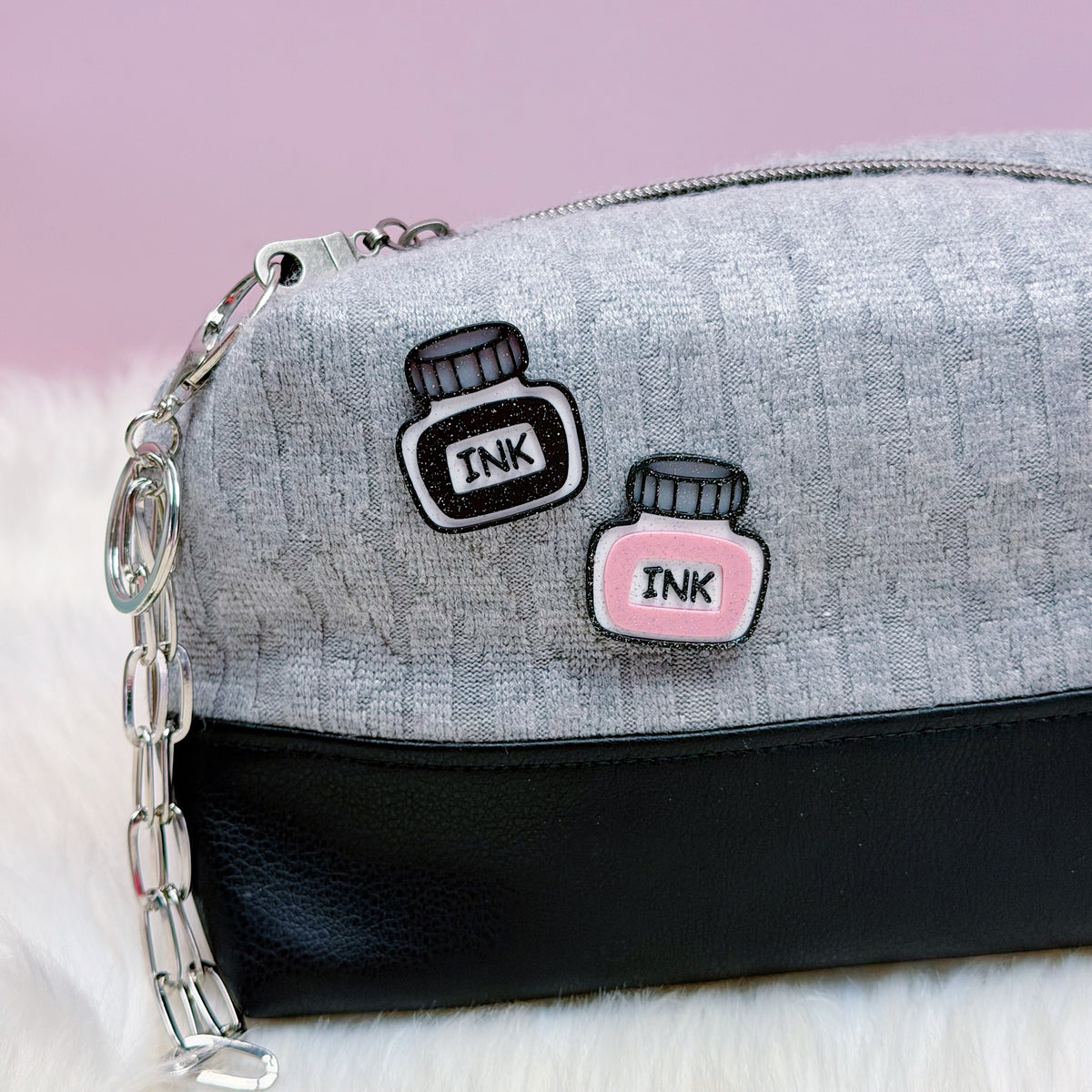 Gray and black pouch with 'INK' bottle pins on a light pink background