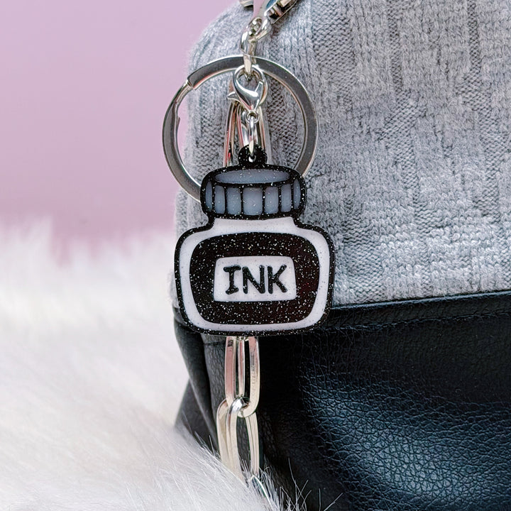 Keychain shaped like an ink bottle attached to a handbag with a pink background