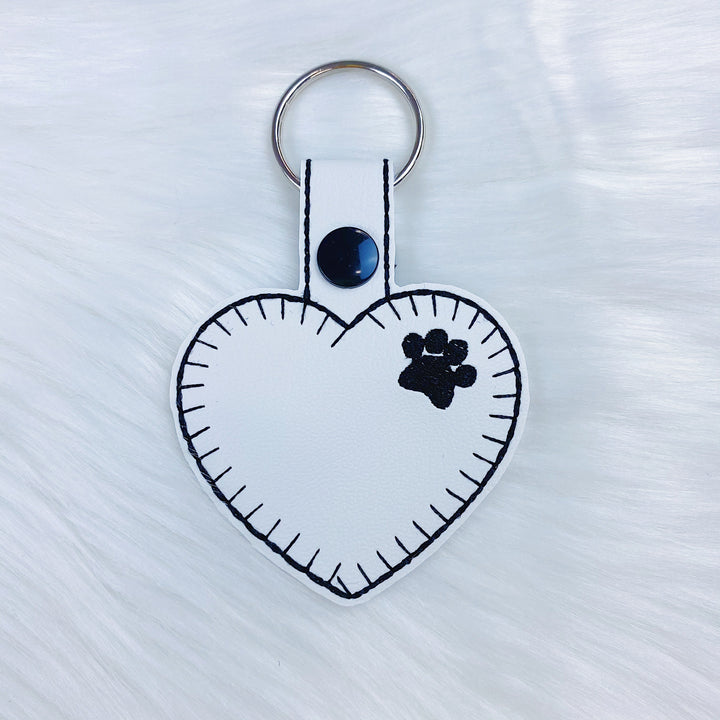 Charm con lengüeta a presión de fieltro de corazón con estampado de pata blanca