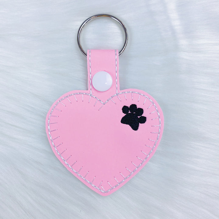 Charm con pestaña a presión de fieltro en forma de corazón con estampado de pata rosa que brilla en la oscuridad